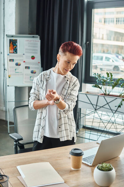 старший менеджер в повседневной одежде, стоящий на рабочем месте и глядя на ноутбук в современном офисе