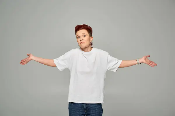 confused and discouraged non-binary person in white t-shirt showing shrug gesture on grey backdrop