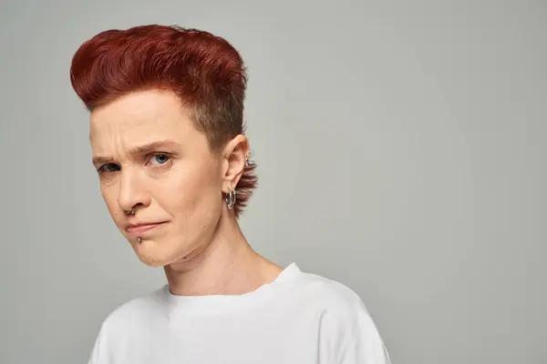 offended and upset redhead non-binary person in white t-shirt looking at camera on grey backdrop