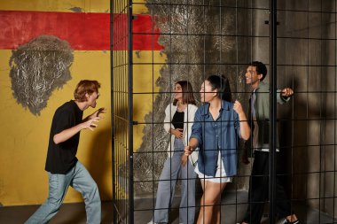 Kızıl saçlı adam kaçış odasında oyun sırasında kilitli kafesin içinde çok kültürlü arkadaşlarını korkutuyor.