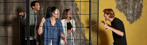 stock image banner of guy scaring his multicultural friends inside of locked cage during game in escape room