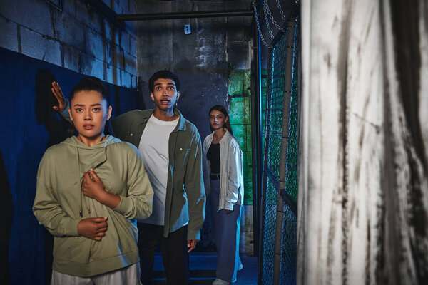 young and interracial friends walking through secret passage in quest room, adventure and mystery