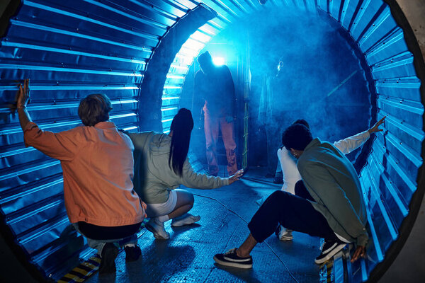 Молодая группа людей сидит в туннеле и смотрит на страшных людей в противогазе, ходящих в дыму