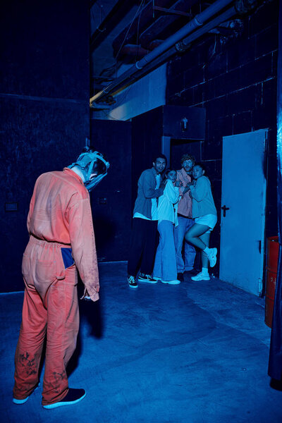 человек в газовой мачте, стоящий рядом с испуганной мультикультурной группой людей в комнате побега, приключения