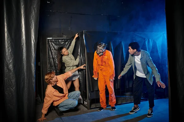 stock image group of multiethnic young people engaged in thrilling escape room hiding from man in ppe suit