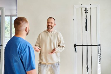 Pozitif adam rehabilitasyon merkezindeki randevu sırasında mavi üniformalı doktorla konuşuyor.