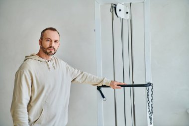 Modern kineziyoloji merkezinin spor salonunda kameraya bakan sakallı yakışıklı adam.