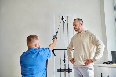 Genç iyileşme uzmanı egzersiz makinesinde çalışıyor, Kinesio Merkezi 'ndeki adamın talimatı.