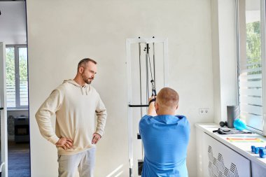 Adam Kineziyoloji Merkezi 'nde egzersiz makinesi eğitimi alan mavi üniforma uzmanına bakıyor.
