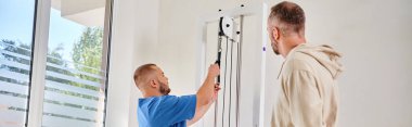 Mavi üniformalı rehabilitolog Kinesio Center 'daki adama eğitim ekipmanı gösteriyor.