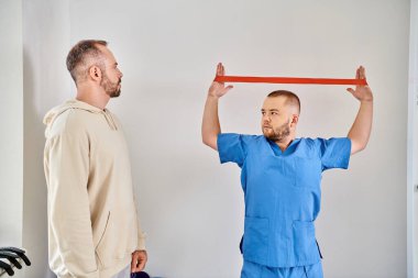 Genç yetenekli fizyoterapist Kinesio merkezinde direniş bandıyla kol egzersizi yapıyor.