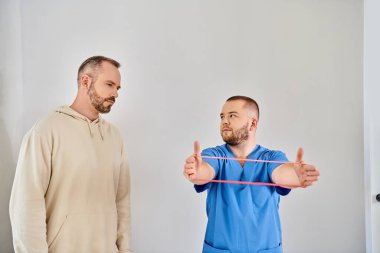 Profesyonel iyileşme uzmanı Kinesio merkezinde direniş bandıyla kol egzersizi yapıyor.