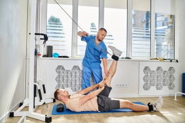 Kinesio Center spor salonunda egzersiz makinesinde çalışan bir adama yardım etme konusunda tecrübeli.