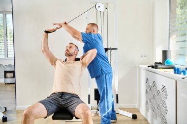 Kinesio Merkezi 'ndeki egzersiz makinesi eğitimi sırasında genç eğitmen adama yardım ediyor.