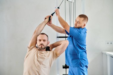 Kinesio Center spor salonunda egzersiz makinesinde çalışan bir adamı destekleyen profesyonel eğitmen