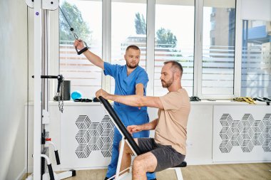 Kinesio Merkezi 'ndeki genç doktorun yanında spor kıyafetleri eğitimi alan erkek hasta.