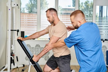 experienced physiotherapist helping man in sportswear during recovery training on exercise machine clipart