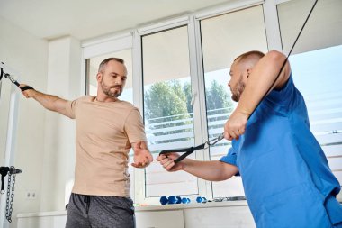 Mavi üniformalı bir asistan Kinesio merkezinde egzersiz makinesi eğitimi için adam hazırlıyor.