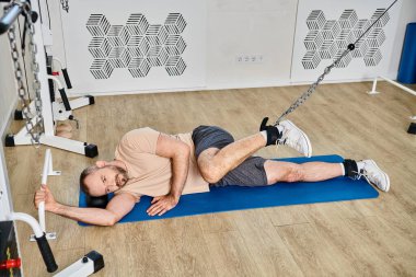 high angle view of man lying down on fitness mat and training on exercise machine in kinesio center clipart