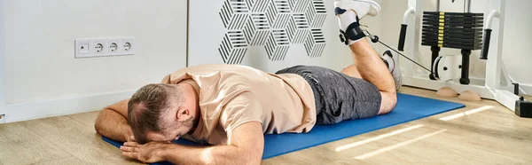 man lying face down on fitness mat and training on exercise machine in kinesio center, banner