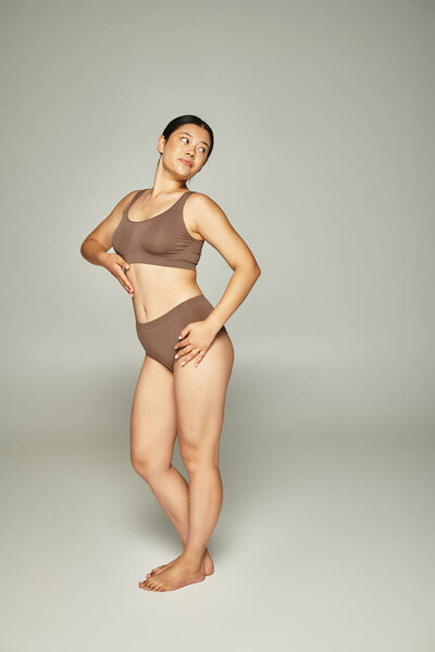 full length of pretty young asian woman in beige underwear posing on grey neutral background