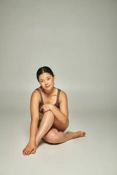 灰色の背景に十字の足で座っている下着の若いアジアの女性の全長 — ストック写真