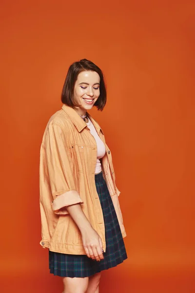 carefree young woman with short hair looking at camera and smiling on orange background, emotion