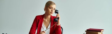 Kırmızı ceketli çekici bir kadın masada oturuyor ve ofisteki retro telefonun başında konuşuyor.