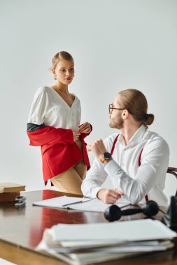 beautiful woman taking off her vibrant red jacket in front of her young bearded boss, work affair clipart