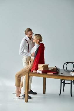 alluring elegant couple with stylish accessories kissing on table while in office, work affair clipart