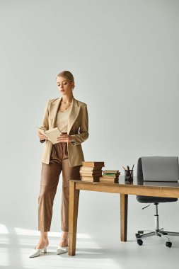 Masanın yanındayken şık takım elbiseli, kitap okuyan güzel bir bayan manken.