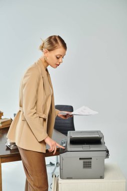 appealing young woman with collected blonde hair using copy machine while working in office clipart