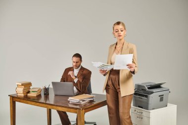 appealing young woman in elegant suit looking at paperwork next to her boyfriend working at laptop clipart