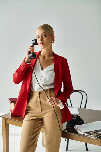 stock image alluring young woman in red jacket talking by vintage phone while working hard in her office