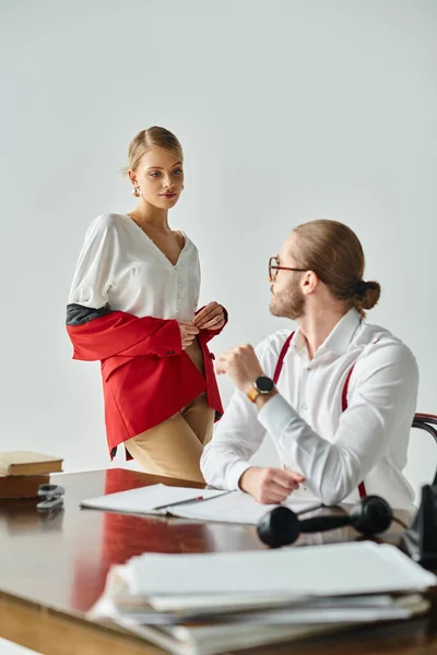 stock image beautiful woman taking off her vibrant red jacket in front of her young bearded boss, work affair