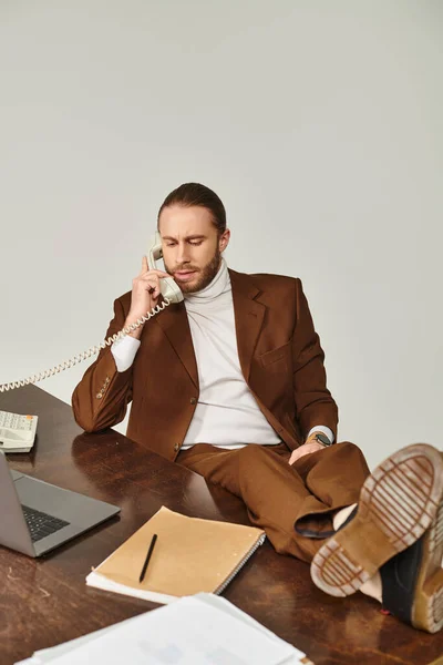 stock image attractive hard working man with beard in brown suit talking by retro phone with legs on table