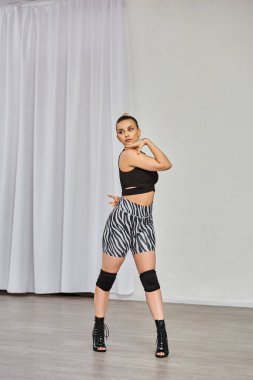 Yüksek topuklu dansçı ve zebra desenli şortlu dansçı beyaz duvara karşı dans ediyor, özgüvenini gösteriyor.