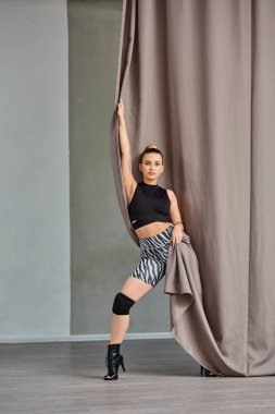 expressive woman in dance clothing and high heels gracefully poses near curtain clipart