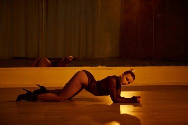 Yüksek topuklu ayakkabılı zarif bir kadın dans stüdyosunda vücudunu cilalı zemine geriyor.