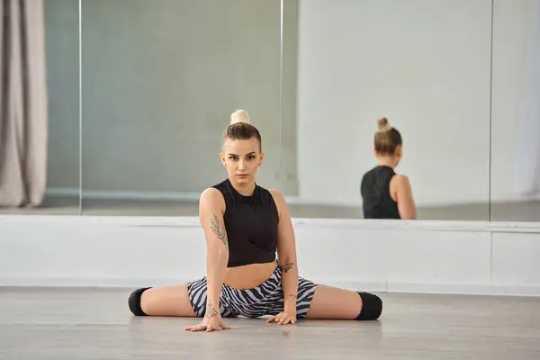 A graceful young woman sits on the flooring, dancer in zebra shorts and a form-fitting top