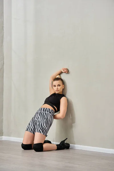 stock image A confident woman strikes a pose against a wall, showcasing her fashionable outfit and high heels