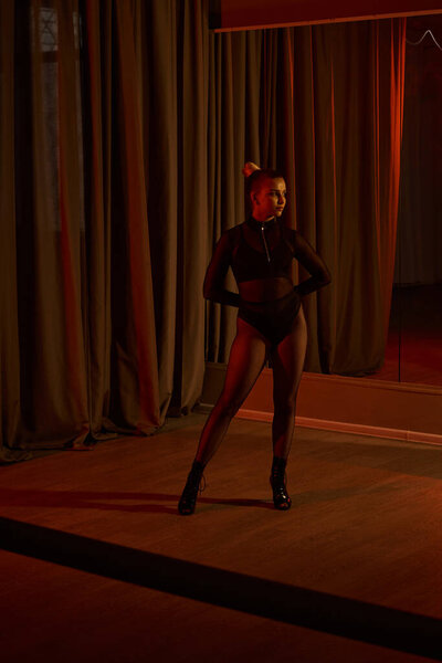 A seductive dancer in a sleek black leotard and fishnet tights gracefully moves behind curtain