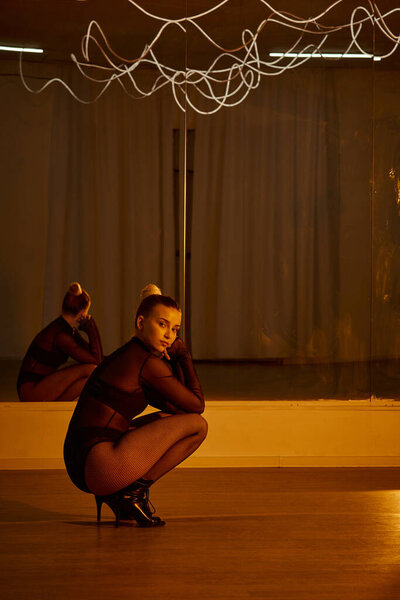 отражение в зеркале красивой женщины в танцевальной одежде и на высоких каблуках, сидящей на танцполе