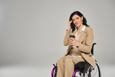 Pastel renkli, zarif giyimli tekerlekli sandalyede oturan, elinde kahve tutan, engelli, güzel görünümlü kadın.