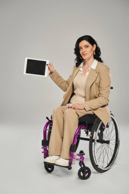 Tekerlekli sandalyedeki hareketli engelli çekici kadın elinde tabletle kameraya bakıyor.
