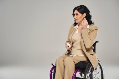 Tekerlekli sandalyedeki pastel kıyafetli güzel engelli kadın gri arka planda kulaklıklarını takıyor.