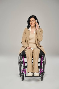 Tekerlekli sandalyede özürlü neşeli, çekici bir kadın telefonla konuşuyor ve kameraya bakıyor.