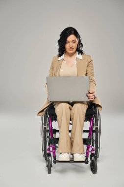 Tekerlekli sandalyesinde oturan ve dizüstü bilgisayarı üzerinde çalışan hareketli engelli çekici bir kadın.