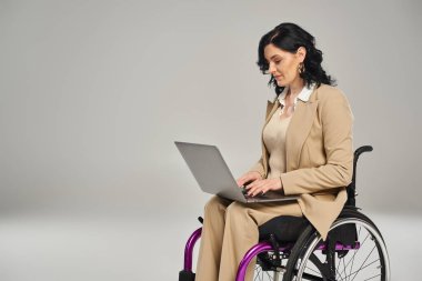 Tekerlekli sandalyedeki kendine güvenen, pastel giyimli ve dizüstü bilgisayarı üzerinde çalışan güzel bir kadın.