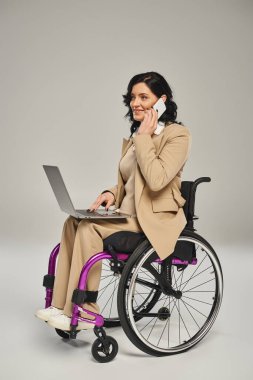 Tekerlekli sandalyede dizüstü bilgisayarıyla yürüyen ve telefonla konuşan neşeli bir kadın.